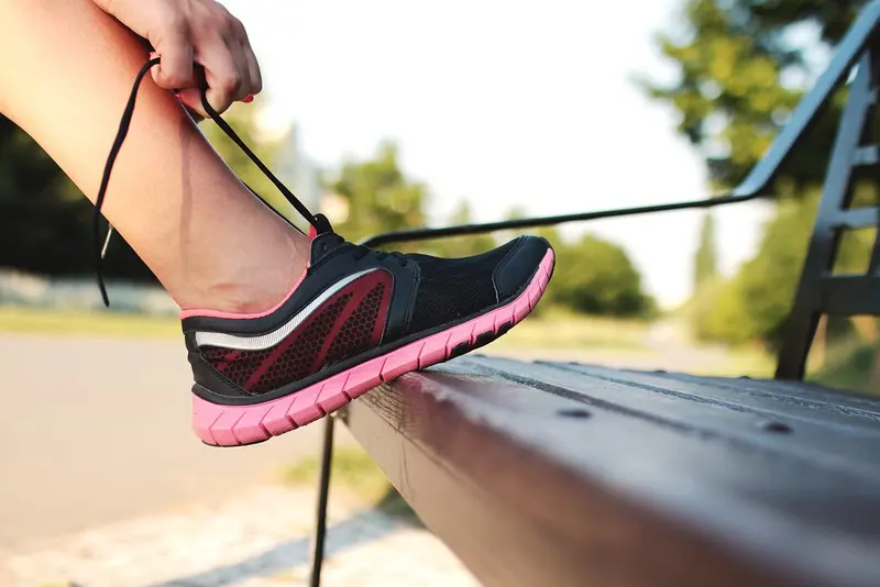 Close-up of a foot on a park bench as a runner ties the laces of a black and pink trainer